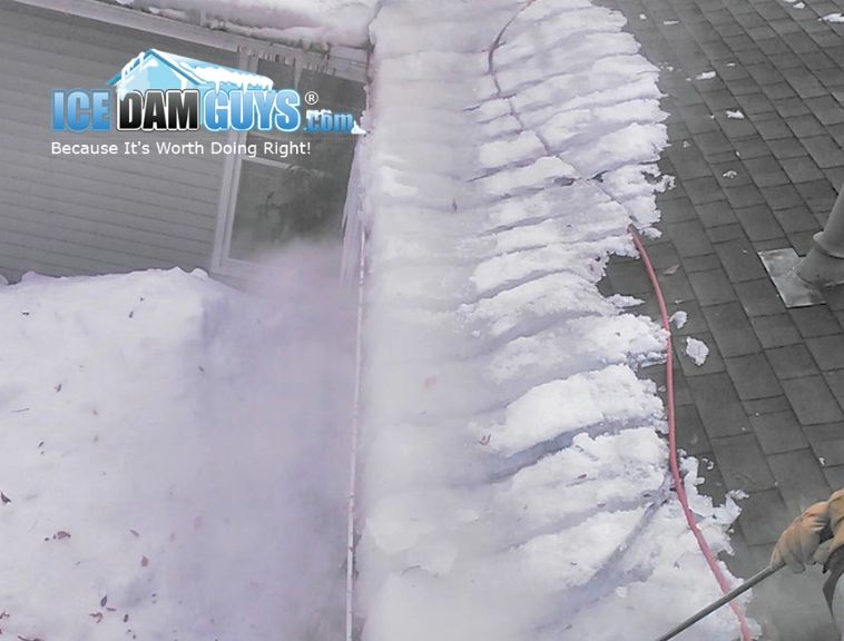 This image shows an Ice Dam Guys technician on a roof. They are removing an ice dam that expands the entire length of the roof by using steam. This hot steam cut through the ice dam easily and the tech now has much smaller pieces to remove more easily.