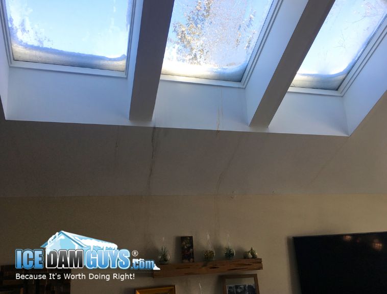 This photo shows three skylights in a home. They have snow on them and unfortunately, streaks of strained water are leaking down their walls. It looks like the sealing or the weight of snow and ice made the skylights weak.