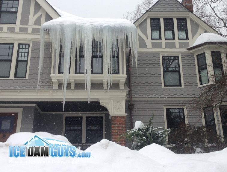 This photo shows a three story home, possibly Victorian, with massive icicles hanging from the roof and an ice dam. These extend past 6 feet in length and need professional attention. 