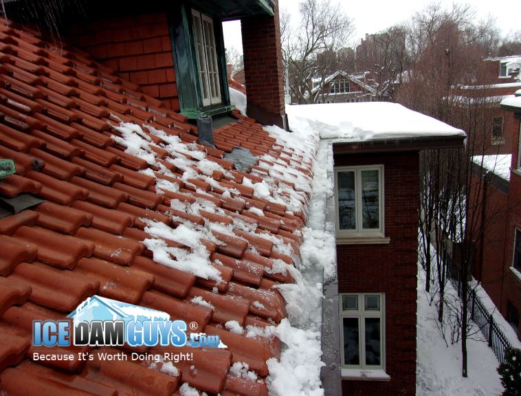 This photo shows a historic home with old clay tiles and copper gutters. The house is ornate and covered in ice dams at the gutters.