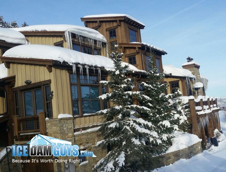 The Ice Dam Guys remove ice dams from vacation rentals like the lodge in this photo. It's a multi-unit property that has significant ice and snow on the roof. It has evergreens around it and looks to be a resort near nature.